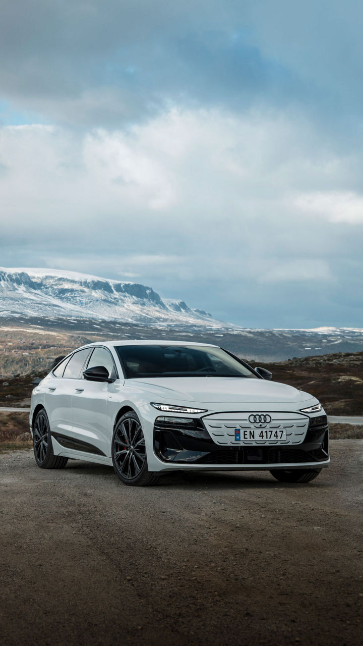Weißer Audi A6 Sportback e-tron vor einer skandinavischen Naturkulisse mit Nadelwäldern, schneebedeckten Bergen und einem Flusslauf.