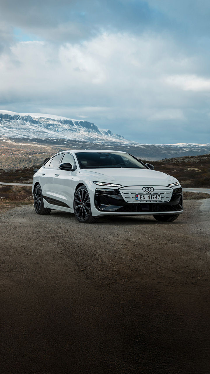 White Audi A6 Sportback e-tron in front of a Scandinavian natural backdrop with coniferous forests, snow-covered mountains and a river.