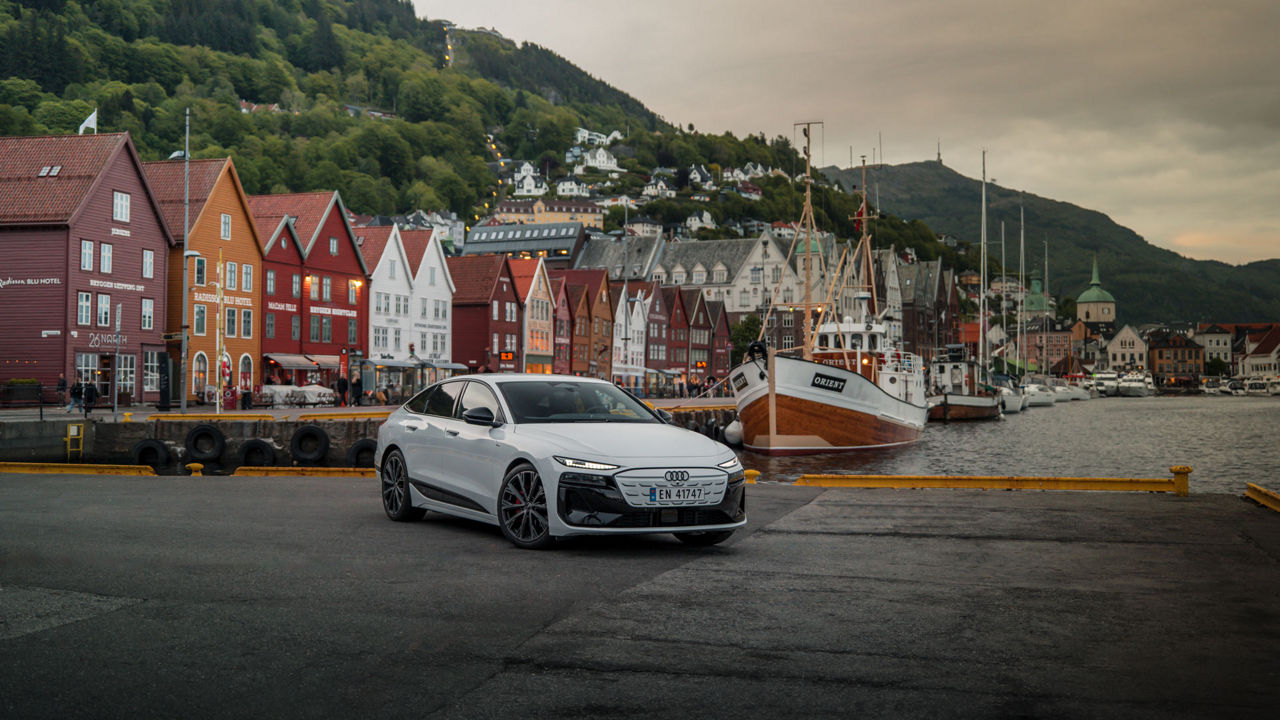 Weißer Audi A6 Sportback e-tron parkt vor einem Kutter. Im Hintergrund pittoreske bunte Häuschen.