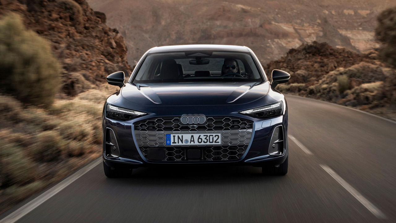 Front view of an Audi A6 driving on a desert road. The side air intakes and the aerodynamic design of the bonnet are clearly visible.