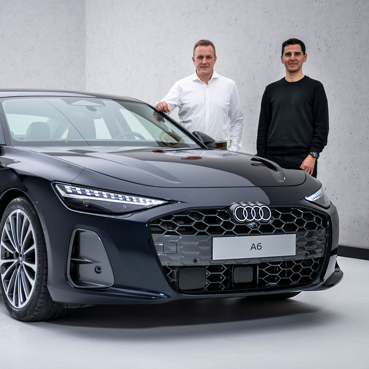 Sebastian Weiper and Francesco d’Amore stand next to the hood of a black Audi A6 Sedan.