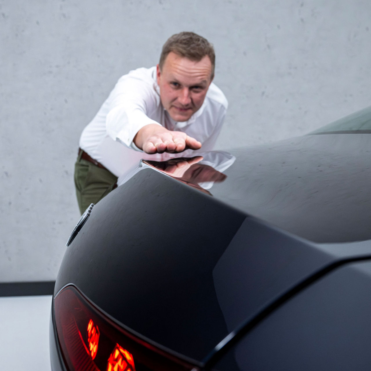 Sebastian Weiper, wearing a white shirt, stands slightly bent over behind the rear of the black Audi A6 saloon, admiring the aerodynamic design with his hand and his eyes.