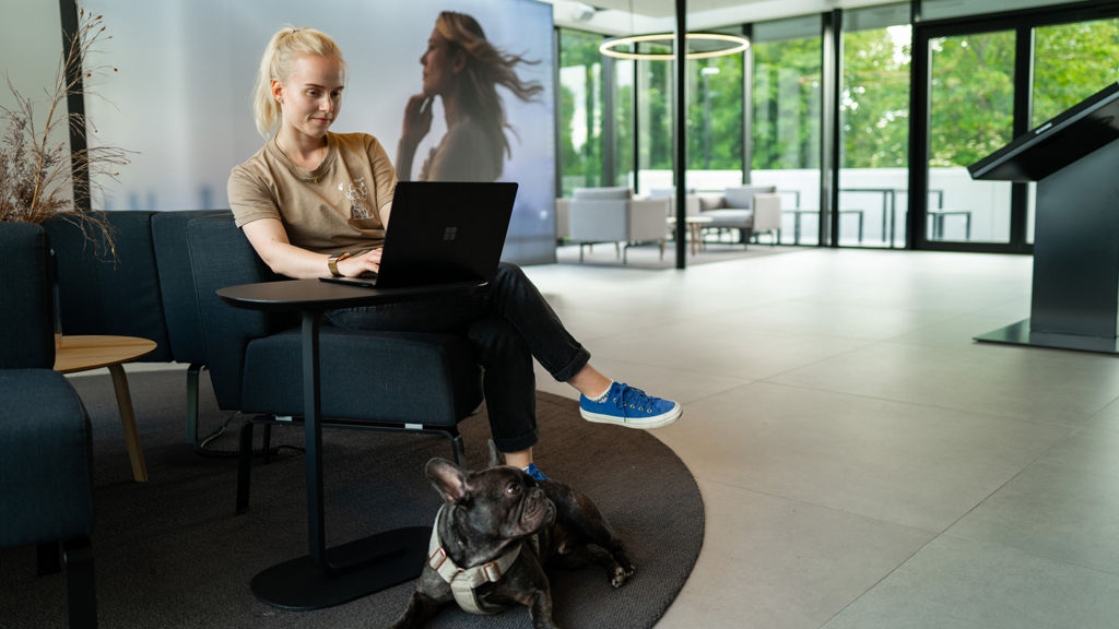 Eine Frau sitzt im Charging hub an ihrem Laptop mit ihrem Hund unterm Tisch