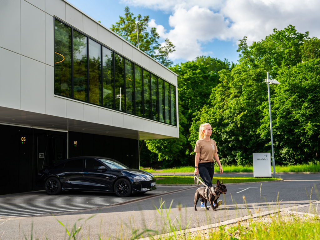 Eine Frau geht mit ihrem Hund an der Leine vom Charging hub weg 