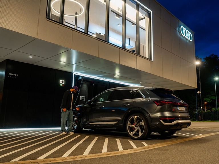 Ein Mann lädt sein Auto am Charging hub bei Nacht