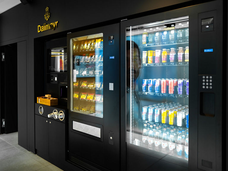 Ein schwarzer Automat mit Snacks und Drinks und dem goldenen Dallmayr Logo