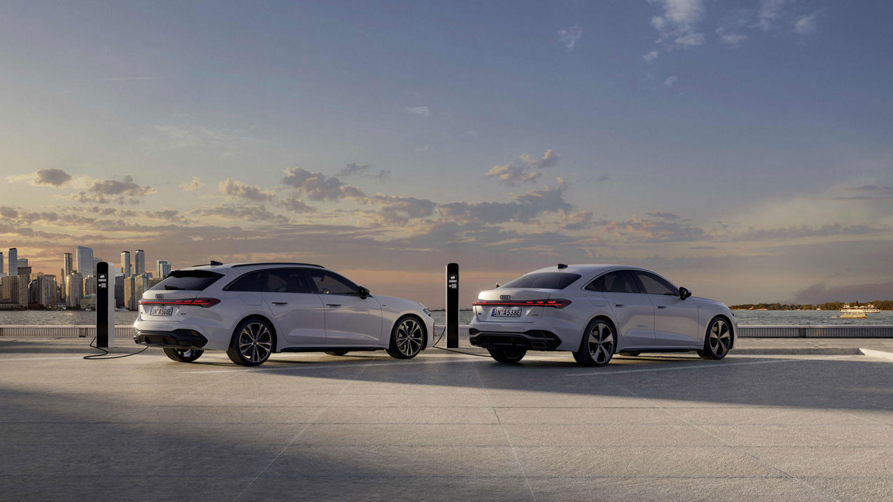 Audi A5 e-hybrid and Audi A5 Avant e-hybrid standing at a charging station, with a cityscape in the distant background
