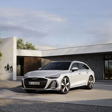 White Audi A6 Avant e-hybrid parked on a concrete slab in front of a modern house with a wallbox.
