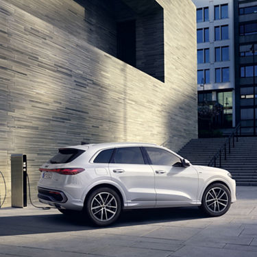 A white Audi Q5 SUV e-hybrid is parked in front of a modern brick house with a charging station.