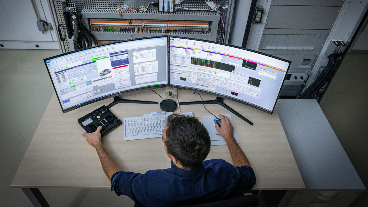 A man sits at a desk in front of two computer screens