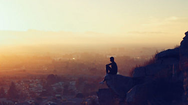 A man sits on a mountain and looks down into the valley 