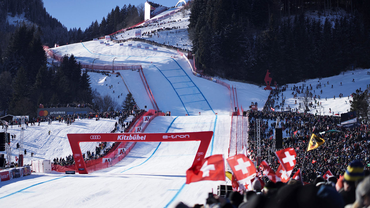 A skier shortly before crossing the finish line in Kitzbühel. An Audi logo and the words Kitzbühel and e-tron can be seen on the red finish arch.