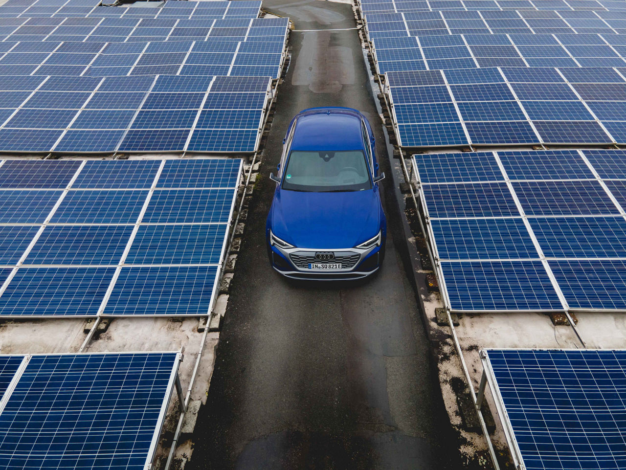 A blue Audi e-tron model stands between photovoltaic systems