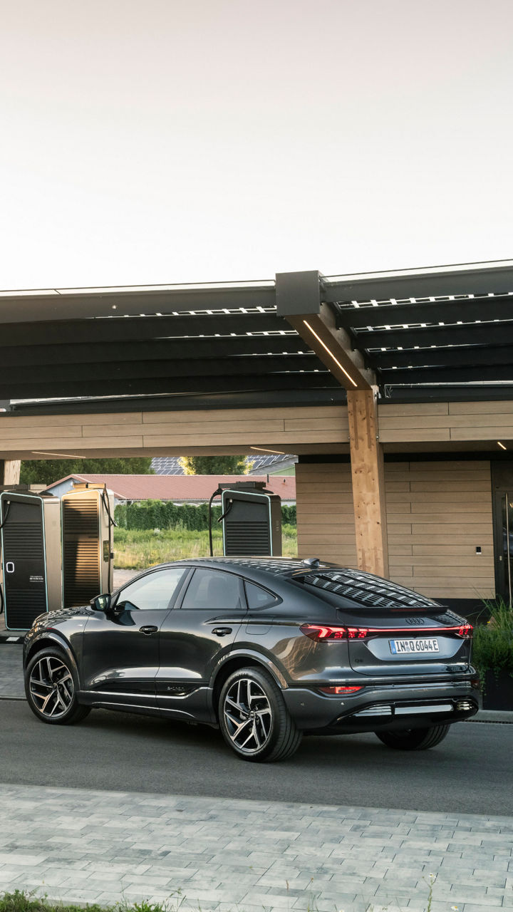 Three Audi SQ6 Sportback e-trons are parked at an Audi Charging Hub. One is charging at a charging station, while the other two are parked on the street in front of it.