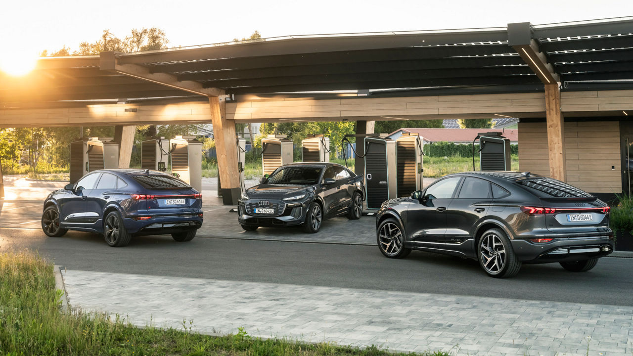Three Audi SQ6 Sportback e-trons are parked at an Audi Charging Hub. One is charging at a charging station, while the other two are parked on the street in front of it.