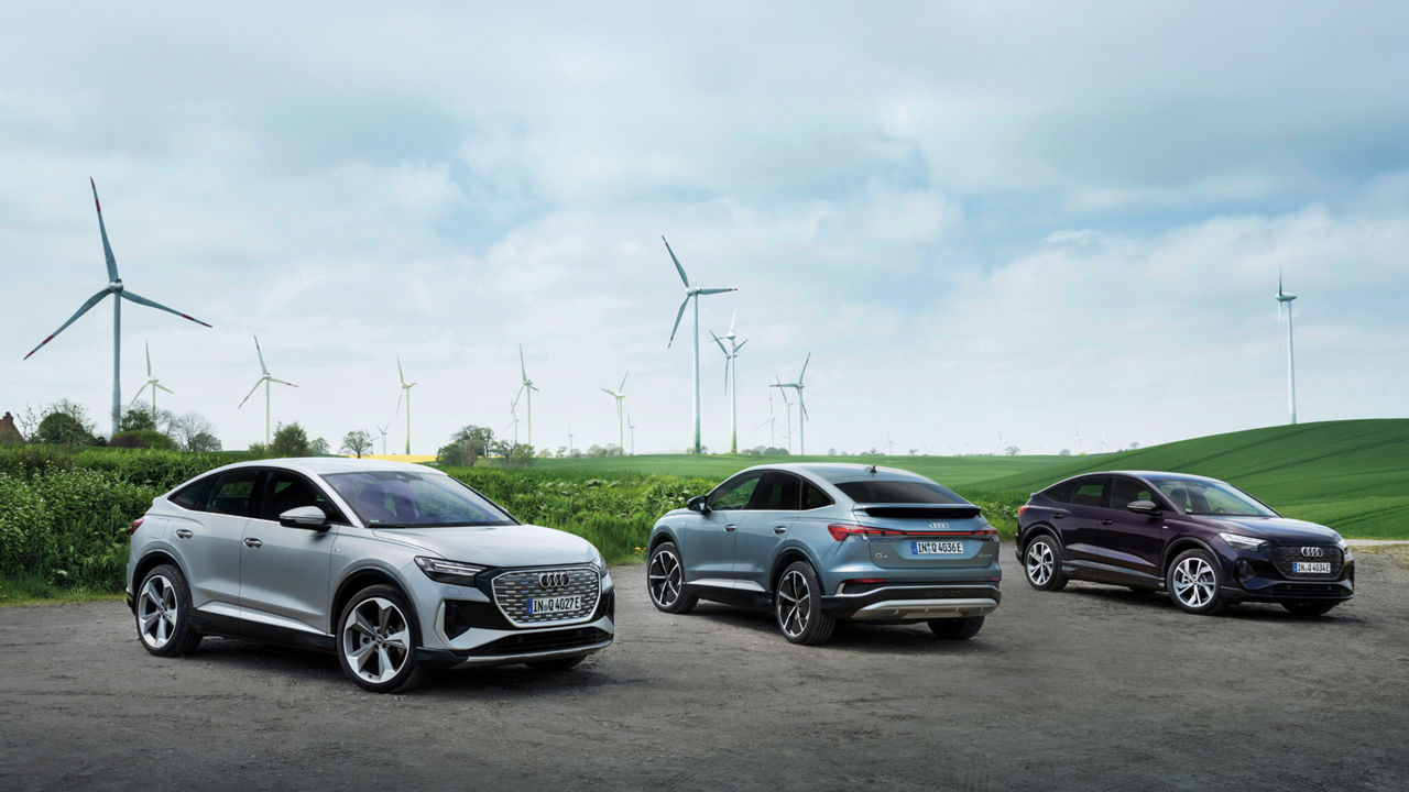 Several Audi Q4 Sportback e-tron models in front of a meadow with wind turbines