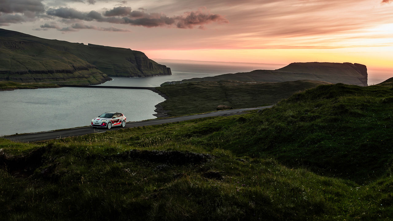 Ein Prototyp Fahrzeug fährt vor einem Sonnenuntergang in einer bergigen Landschaft mit See