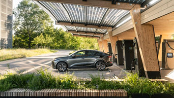 Dark grey Audi Q6 Sportback e-tron charging at a charging station in a wooden-roofed charging station.