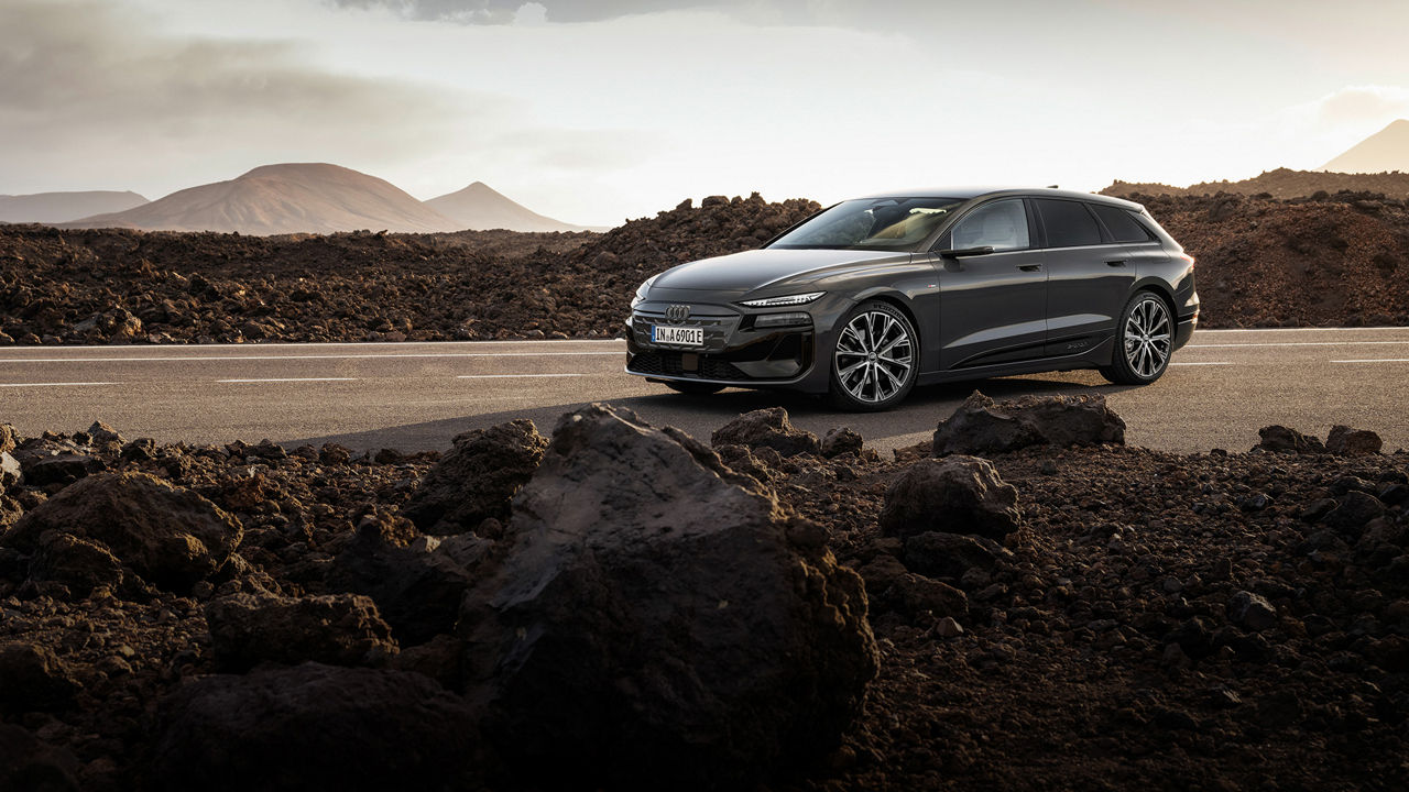 The Audi A6 Avant e-tron performance stands on a road in front of a mountain backdrop. Rocks and rubble lie beside the road. 