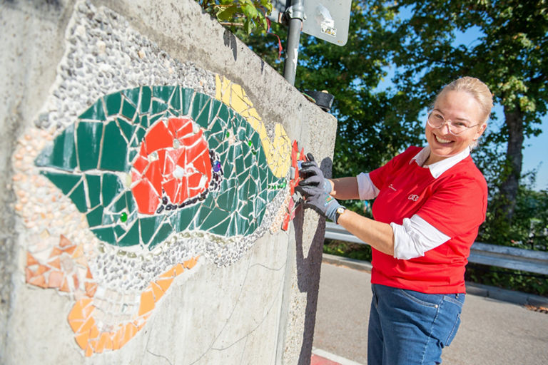 A woman works on a wall with colourful tiles