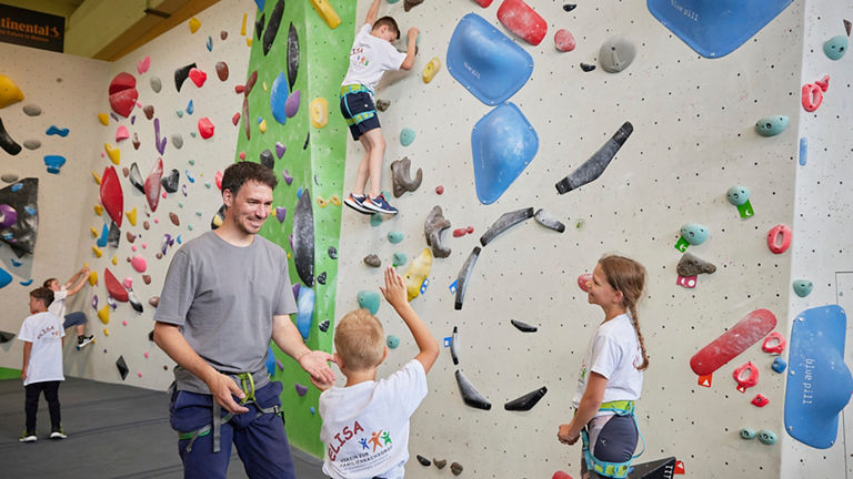 Man high-fiving with children in front of climbing wall.