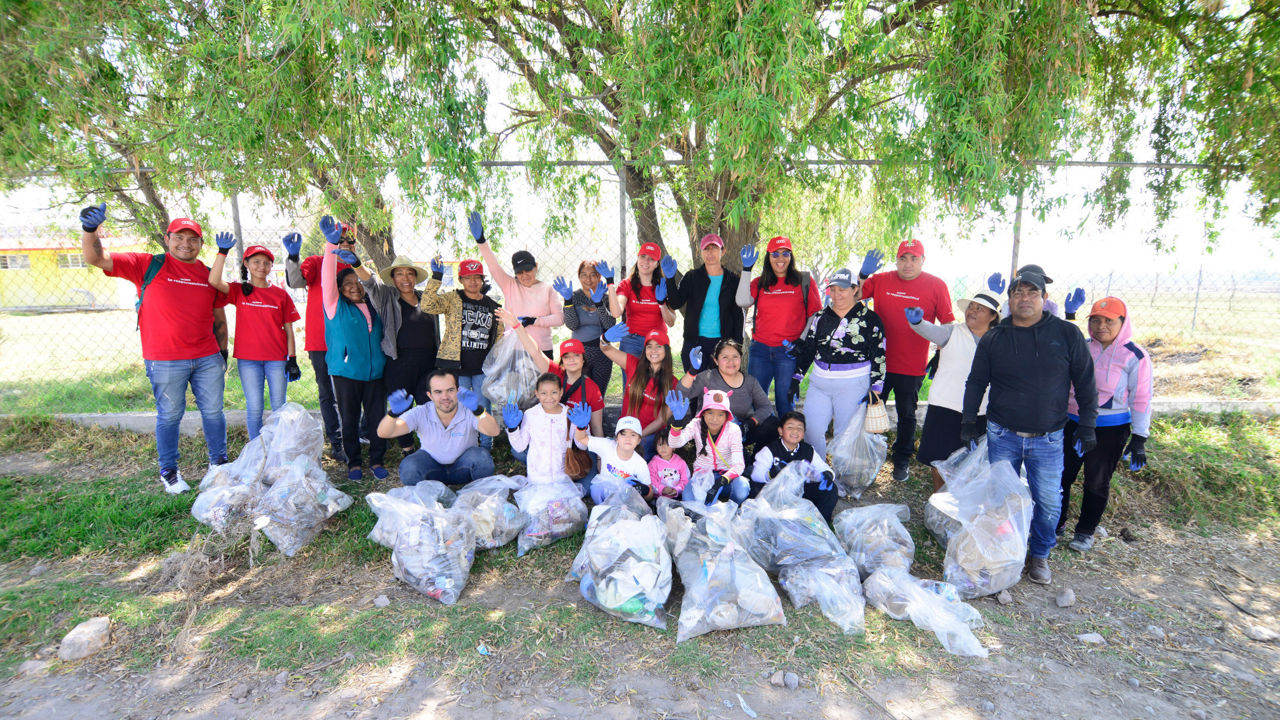 Audi Mexico employees and children wave smilingly into the camera - in front of them lies collected garbage in bags.