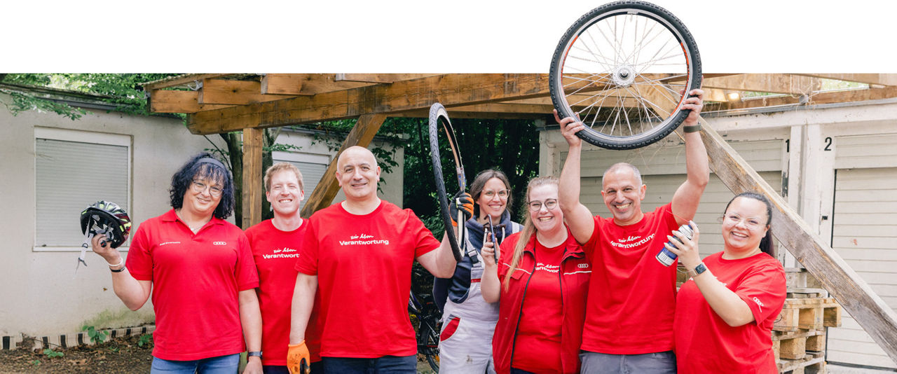 Employees in red T-shirts stand in front of a garage and hold bicycle parts in the air