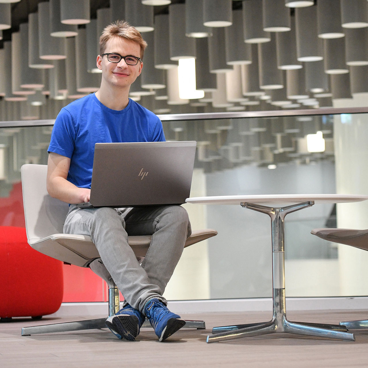 Tim sitzt mit einem Laptop an einem Tisch in der Caffeteria