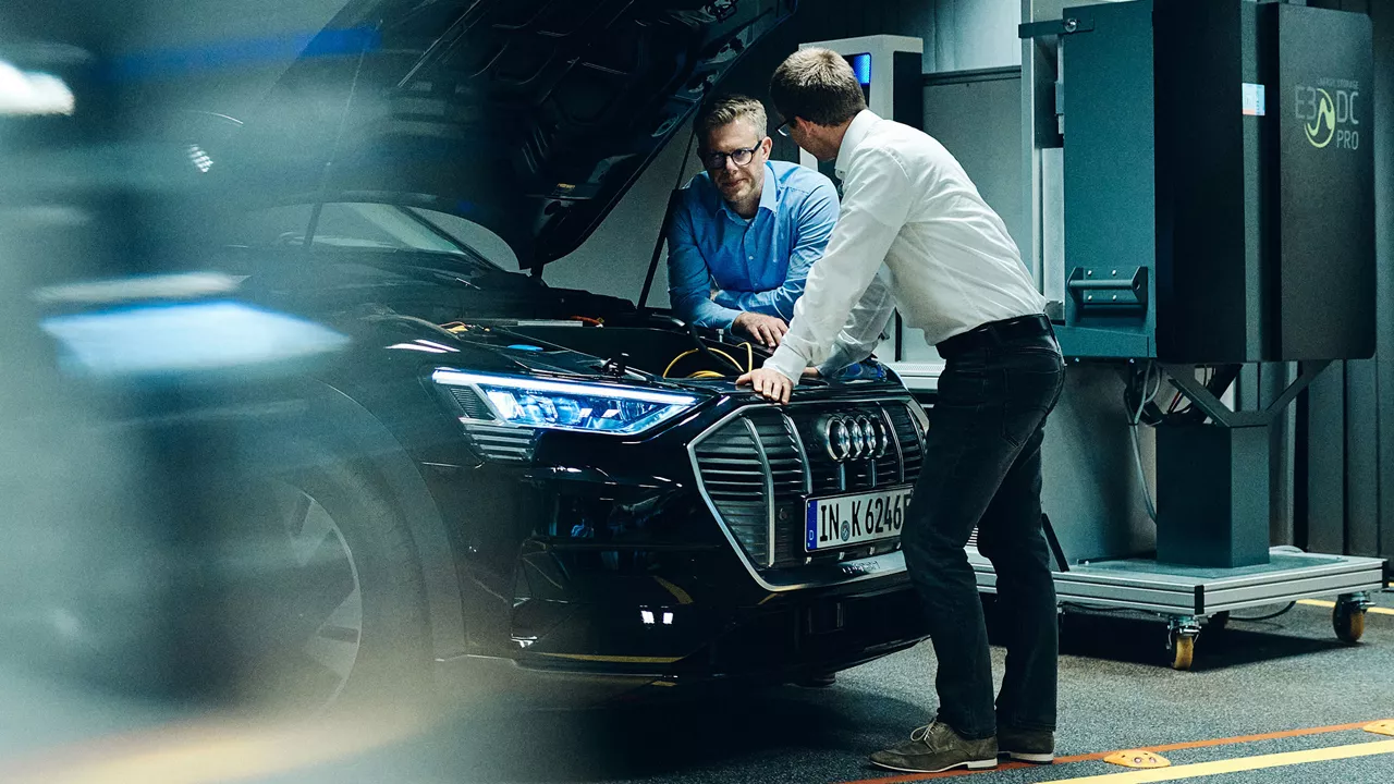 Two employees stand by the open bonnet of an Audi