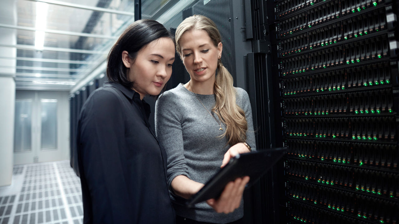 Two employees are standing in a server hall looking at a tablet together
