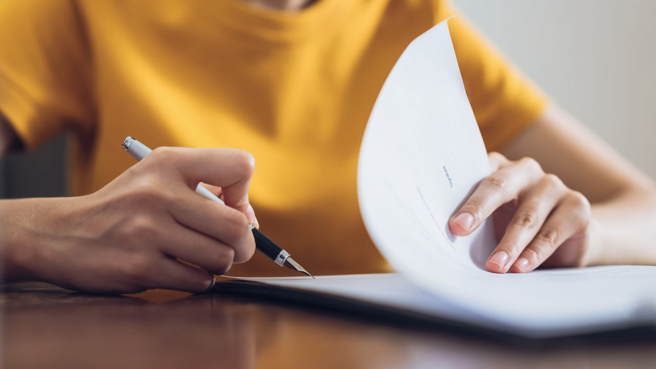 A woman in an orange blouse leafs through and signs a document