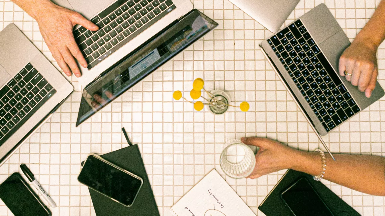 Top view of a desk where several people are working on laptops