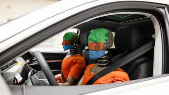 Two dummies sit in the driver and passenger seats of an Audi for a crash test
