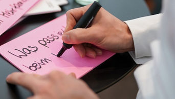 A close-up of a hand writing something on pink paper