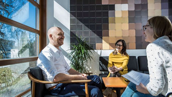 3 people sitting around a table and chatting happily