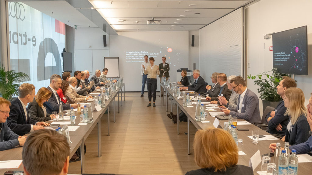 Viele Personen sitzen bei einem Vortrag an einem U-förmigen Tisch
