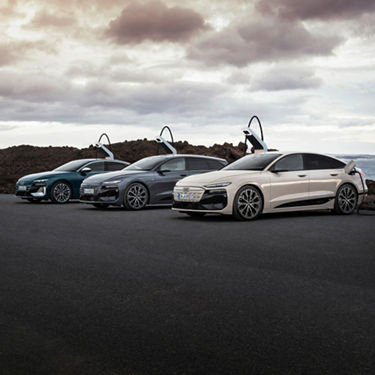 Ein Audi A6 Sportback e-tron performance, Audi A6 Avant e-tron performance und ein Audi S6 Sportback e-tron stehen an Ladesäulen vor dem Meer