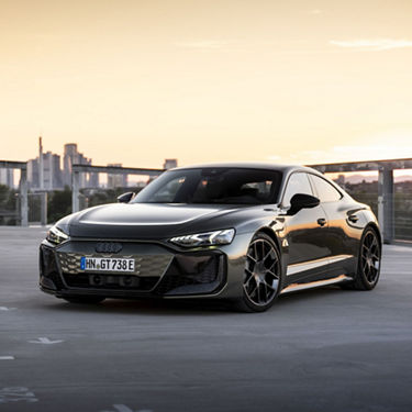 Ein Audi RS e-tron GT performance in Oakgrün Metallic vor einer Skyline im Sonnenuntergang