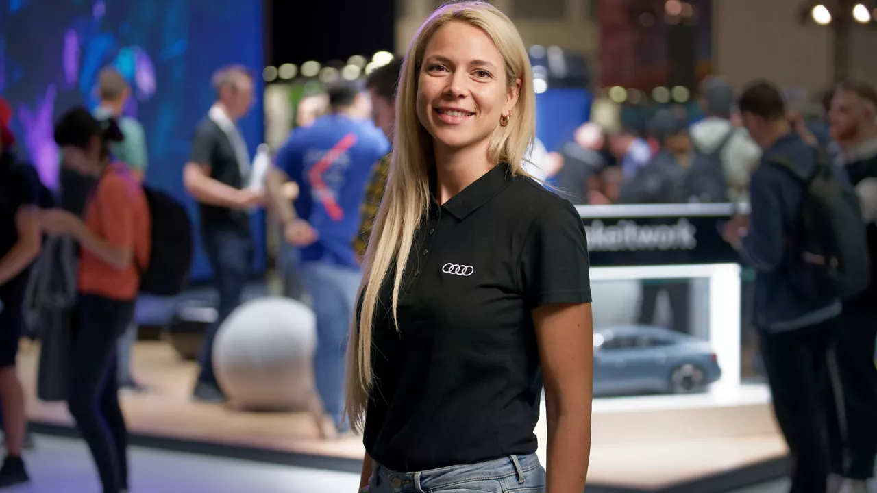 Eine Frau schaut lächelnd in die Kamera und trägt ein schwarzes Shirt mit Audi Logo