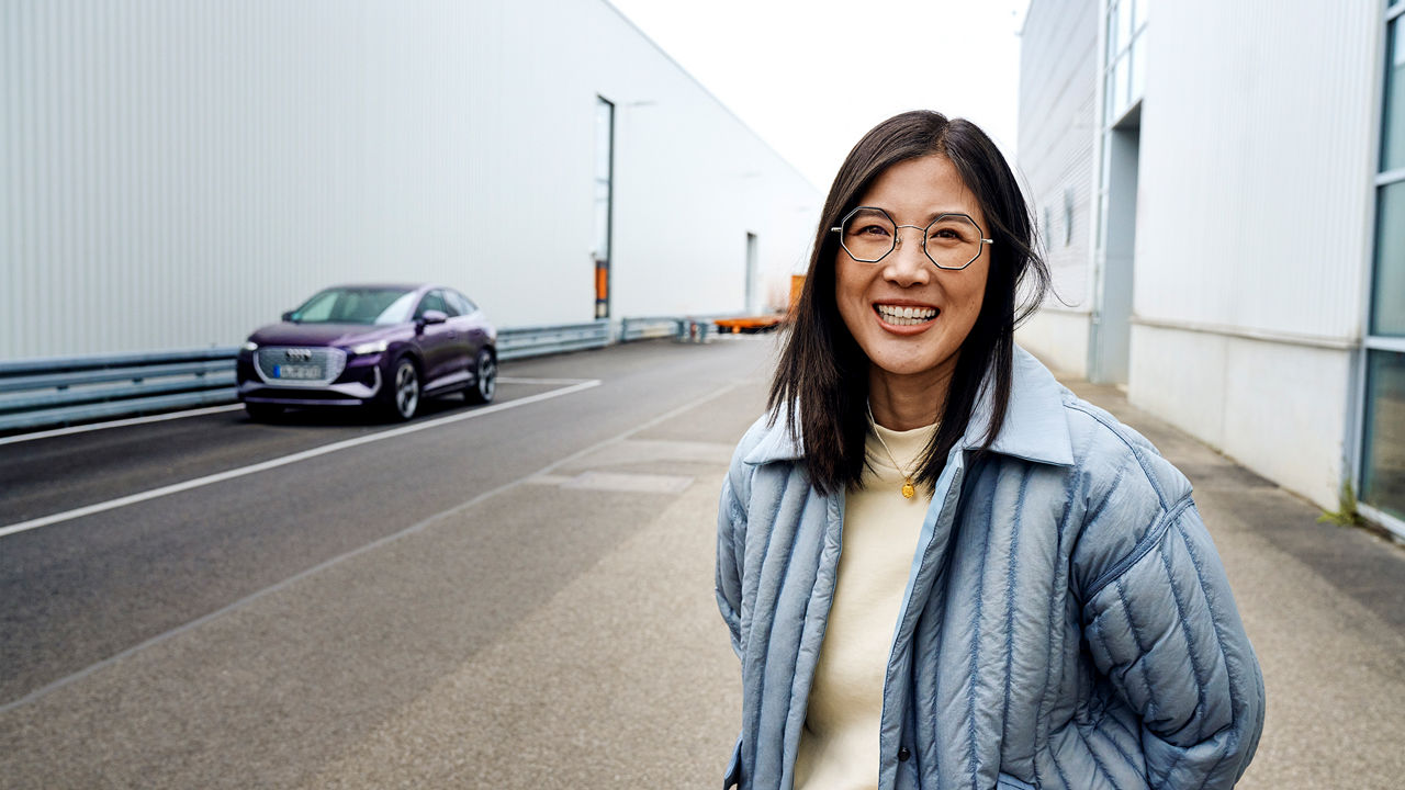 Tiantian steht vor einem lilanen Audi und lächelt in die Kamera