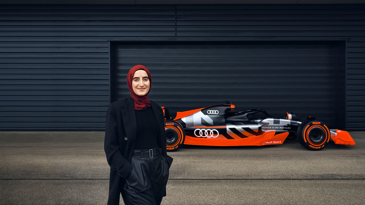 Sümeyye stands in front of an Audi Formula 1 car and smiles into the camera