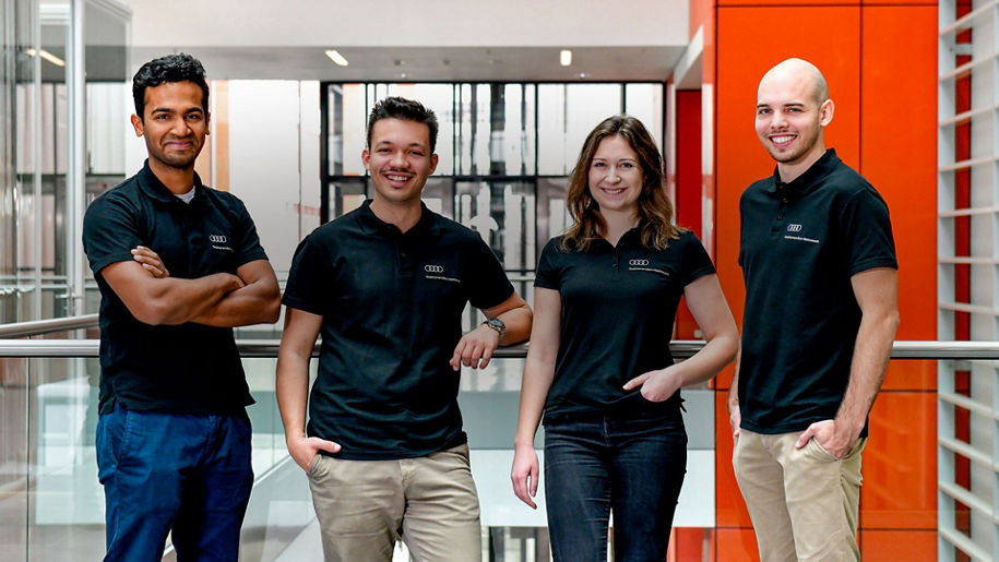 Vier Personen lächeln in die Kamera und tragen dunkle Audi-Shirts