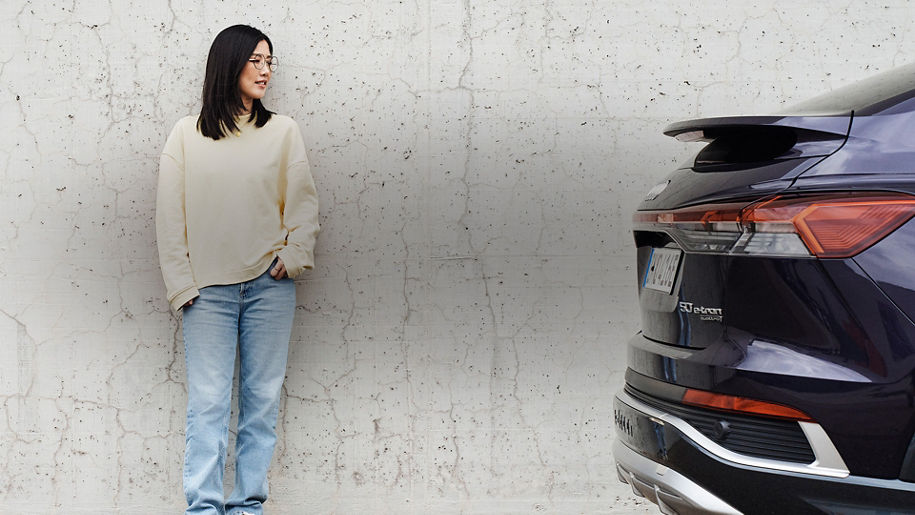 Tiantian steht an einer Wand und schaut nach rechts zu einem lilanen Audi