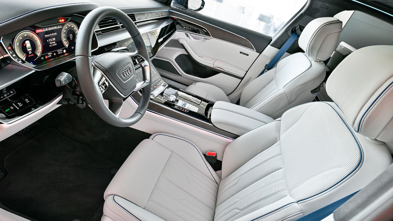 High-quality interior of an Audi A8L with white leather seats, a modern steering wheel and a digital cockpit display.