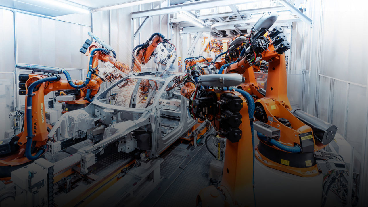 Roboterarme schweißen eine Karosserie in einer hell ausgeleuchteten, automatisierten Fertigungslinie.