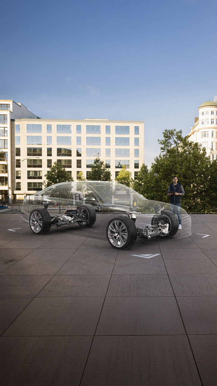 Zwei Männer betrachten ein per Augmented Reality dargestelltes, durchsichtiges Auto mit sichtbarer Technik im urbanen Außenbereich.