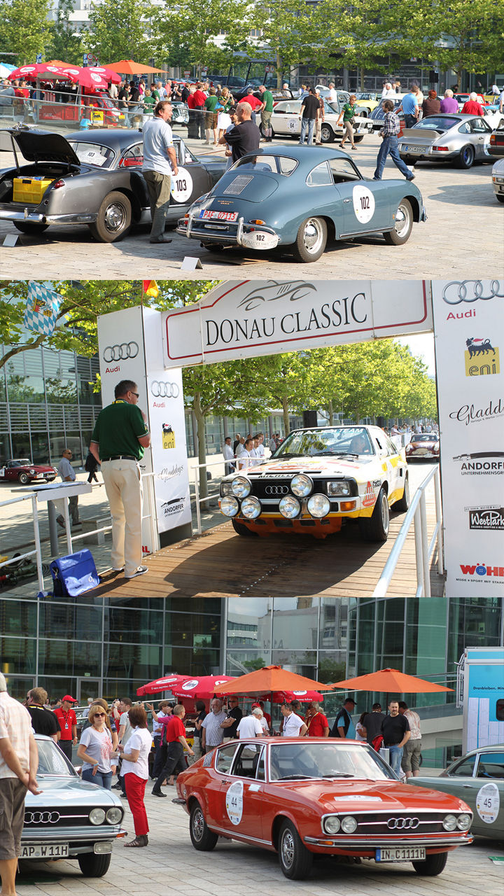 Klassische Fahrzeuge bei der Donau Classic Rallye vor dem Audi Forum, umgeben von Besuchern bei sonnigem Wetter.