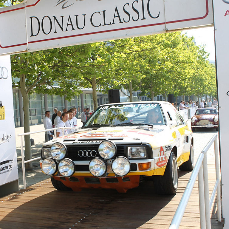 Old timer underneath a sign with "Donau Classic" written on it.