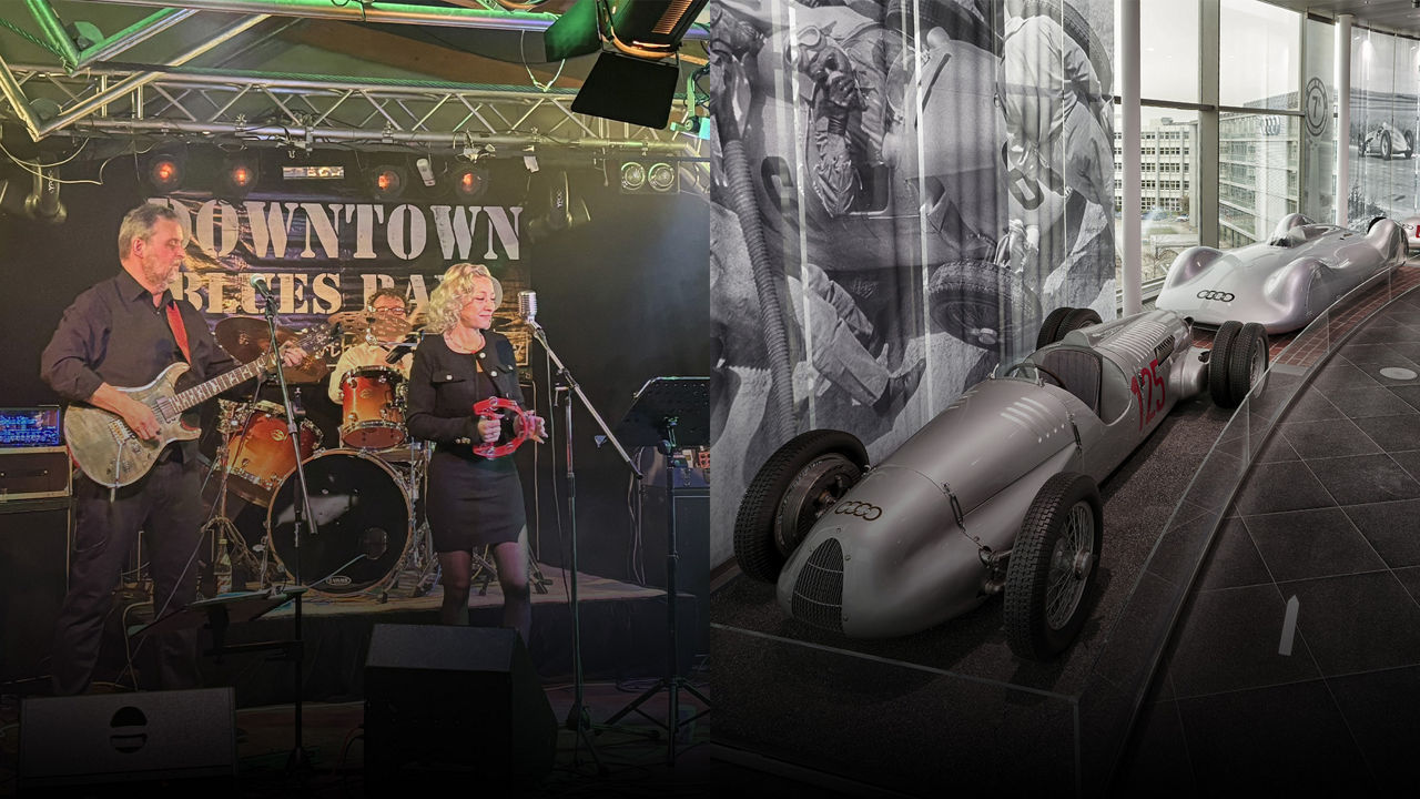 Band auf Bühne mit E-Gitarre, Schlagzeug und Sängerin mit Tamburin beim Auftritt unter dem Banner „Downtown Blues Band“ und zwei silberne historische Audi-Rennwagen.