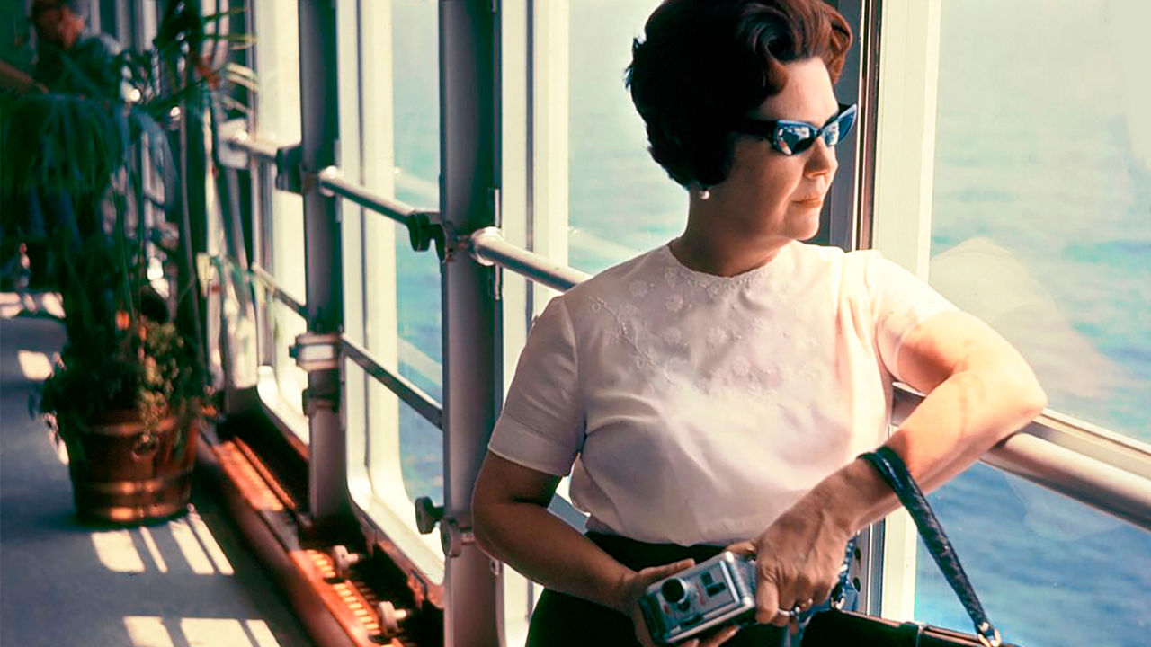 Eine Frau mit Sonnenbrille und einer Kamera in der Hand schaut aus einem Fenster einer hohen Aussicht 